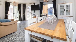 Ein modernes Wohnzimmer mit einem Holzesstisch, weißen Stühlen, einem beigen Sofa und einem großen Fenster mit Vorhängen.