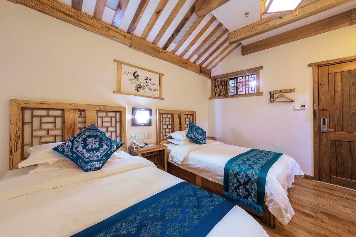 Ein Zimmer mit zwei Betten, Holzbalken an der Decke, einer Holztür und einem kleinen Fenster.