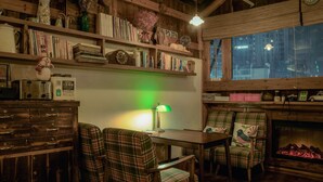 A cozy room with wooden shelves, a table, plaid chairs, a fireplace, and a view of the city at night. - MinGuo Life Zhangjiajie (Zhangjiajie)