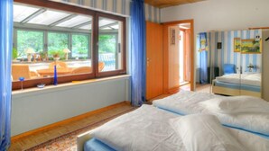 Une chambre avec deux lits, une grande fenêtre avec des rideaux, un plafond en bois et une vue sur la verdure.