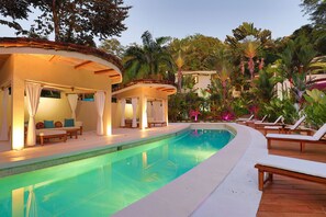 Una piscina con sillas de descanso y una zona de estar cubierta con cortinas.