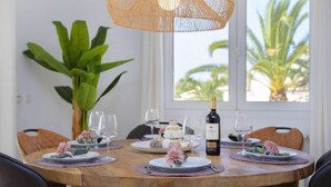 Une table de salle à manger ronde, avec des assiettes, des verres et une bouteille de vin, entourée de chaises et d’une grande plante.