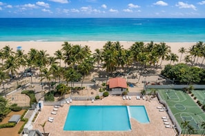 Un complexe hôtelier situé en bord de mer, doté d’une piscine, de courts de tennis et de palmiers.