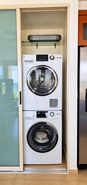 Ein kompaktes, wandmontiertes Wasch- und Trocknergerät mit einer Glasablage darüber, in einer modernen Küchenumgebung.
