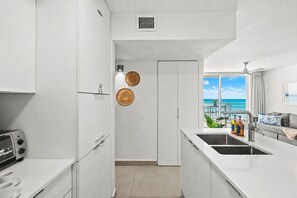 Una cocina moderna con armarios blancos, horno empotrado y ventana con vistas a un balcón sobre el océano.