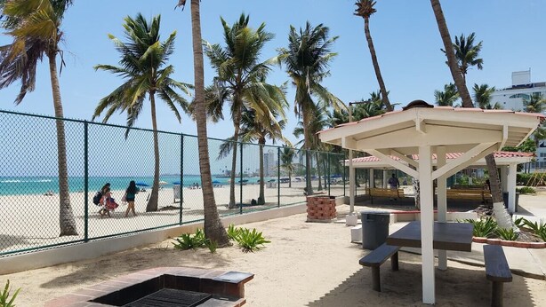 Een terras aan het strand met een barbecue, banken en een overdekte zithoek.