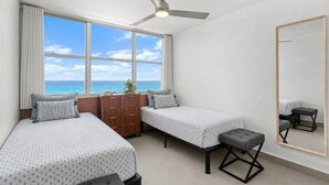 Een slaapkamer met twee bedden, een plafondventilator, een dressoir, een bankje en een grote spiegel.