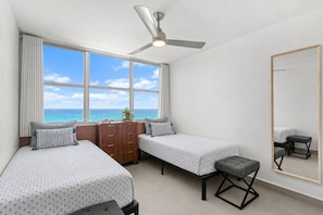 Une chambre avec deux lits, un ventilateur de plafond, une commode, un banc et un grand miroir.