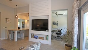 Un salon moderne doté d’un grand téléviseur à écran plat, d’un coin repas et d’un espace détente confortable agrémenté de coussins à motifs.