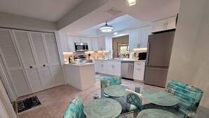 Een moderne keuken met witte kasten, een centraal eiland en een eethoek met glazen tafels en teal stoelen.