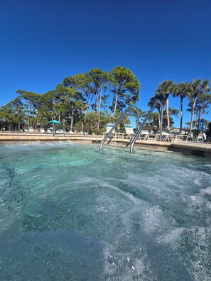 Ein Poolbereich mit klarem Wasser, Liegestühlen und Palmen.