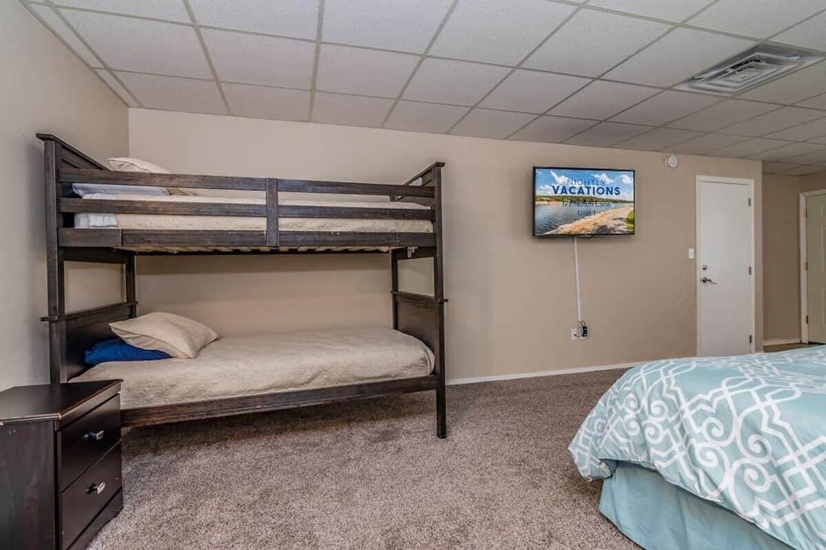 Habitación con literas, un televisor en la pared, una puerta y piso alfombrado.