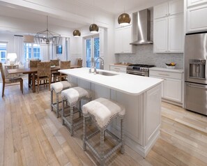 Une cuisine moderne dotée d’un grand îlot central, de tabourets de bar, d’appareils électroménagers en acier inoxydable et d’un coin repas agrémenté d’un lustre.