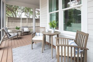 A covered outdoor seating area with a wooden table and chairs, a cushioned bench, and a view of the backyard through large windows.