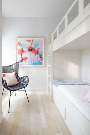 A room with a bunk bed, a chair with a cushion, and a framed painting on the wall.
