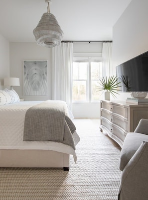 Une chambre à coucher avec un lit, une commode, un téléviseur et une fenêtre avec des rideaux.