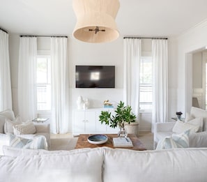 A modern living room with a flat-screen TV, white sofas, a coffee table, and a bookshelf.