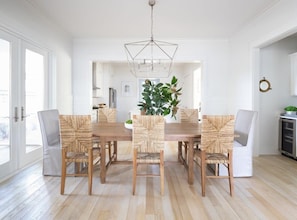 Een eetruimte met een houten tafel en zes stoelen, een hanglamp en een grote plant.