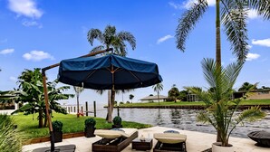Un espace extérieur aménagé avec des meubles en osier, un parasol bleu et une vue sur une étendue d’eau et de la verdure.