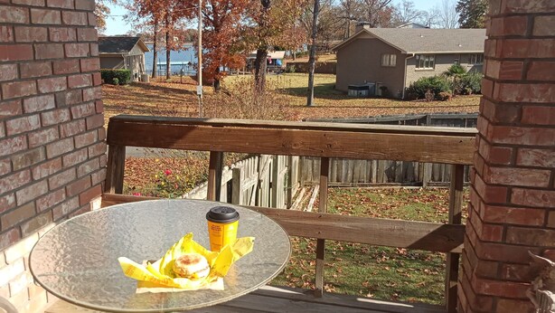 A glass table with a beverage cup and a wrapped item on a balcony with a wooden railing. - Welcome to Polly's Place (Rockwell)