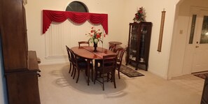 A dining area with a wooden table and chairs, a vase with flowers, a red curtain, and a cabinet with glass doors. - Welcome to Polly's Place (Rockwell)