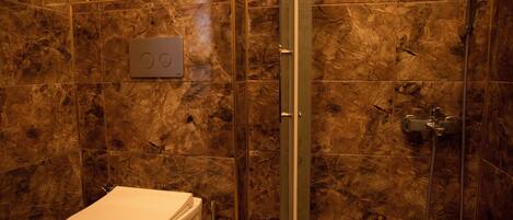 Un baño con inodoro, cabina de ducha y pared de mármol.