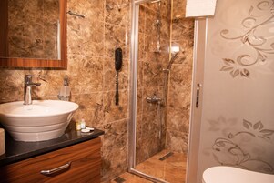 Un baño con lavamanos de mármol, cabina de ducha con paredes de vidrio y un inodoro.