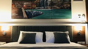 Habitación de hotel con una cama grande, un cabecero y un cuadro colgado en la pared de una cascada.