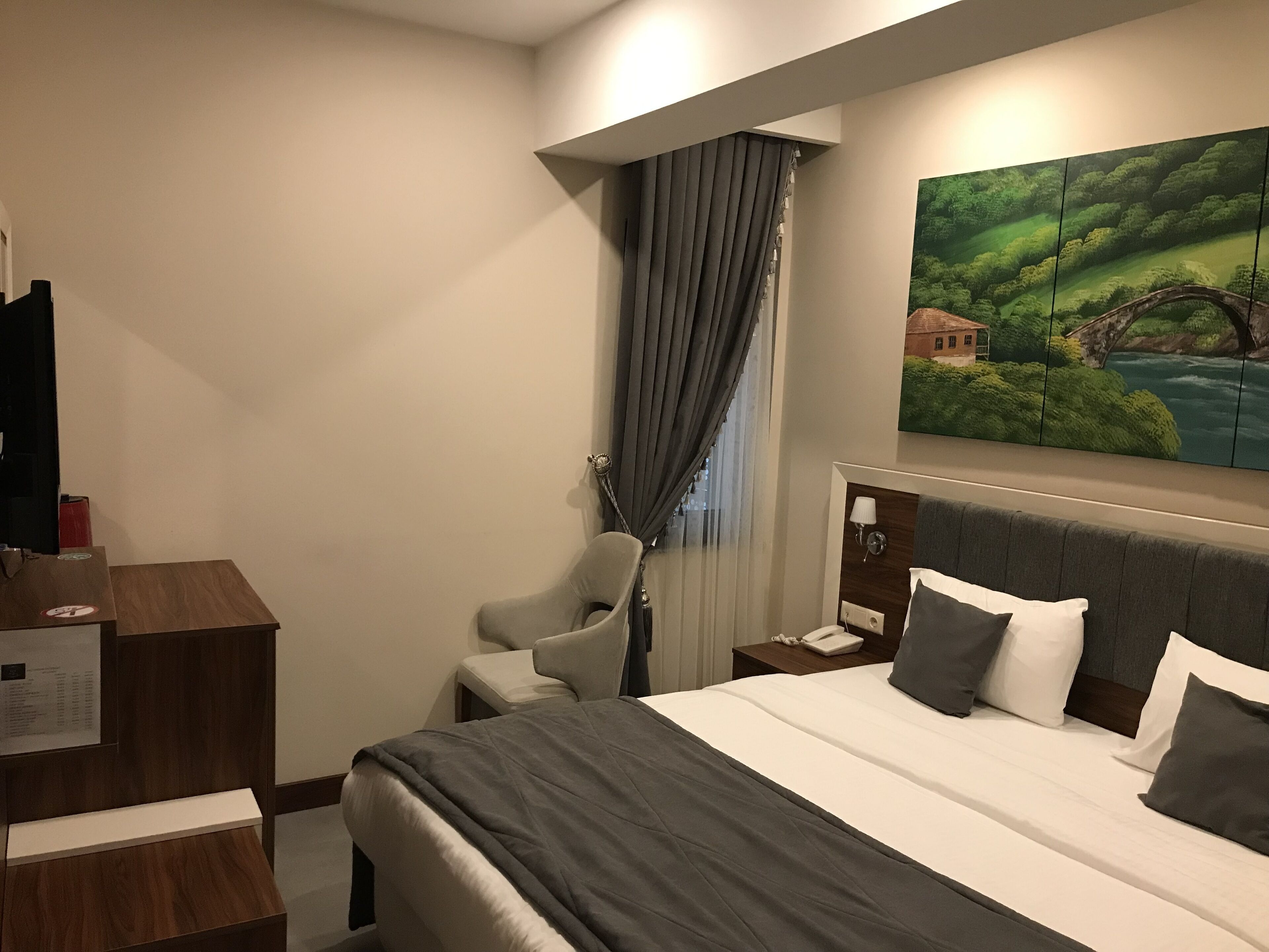 Una habitación de hotel con una cama grande, un escritorio, una silla y un cuadro de un paisaje.