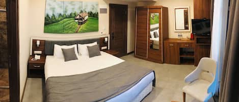 Una habitación de hotel con una cama grande, un escritorio con televisor, una silla, un armario y un cuadro en la pared.