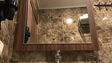 Un baño con piso de mármol, espejo con marco de madera, lavamanos blanco y un perchero para toallas.