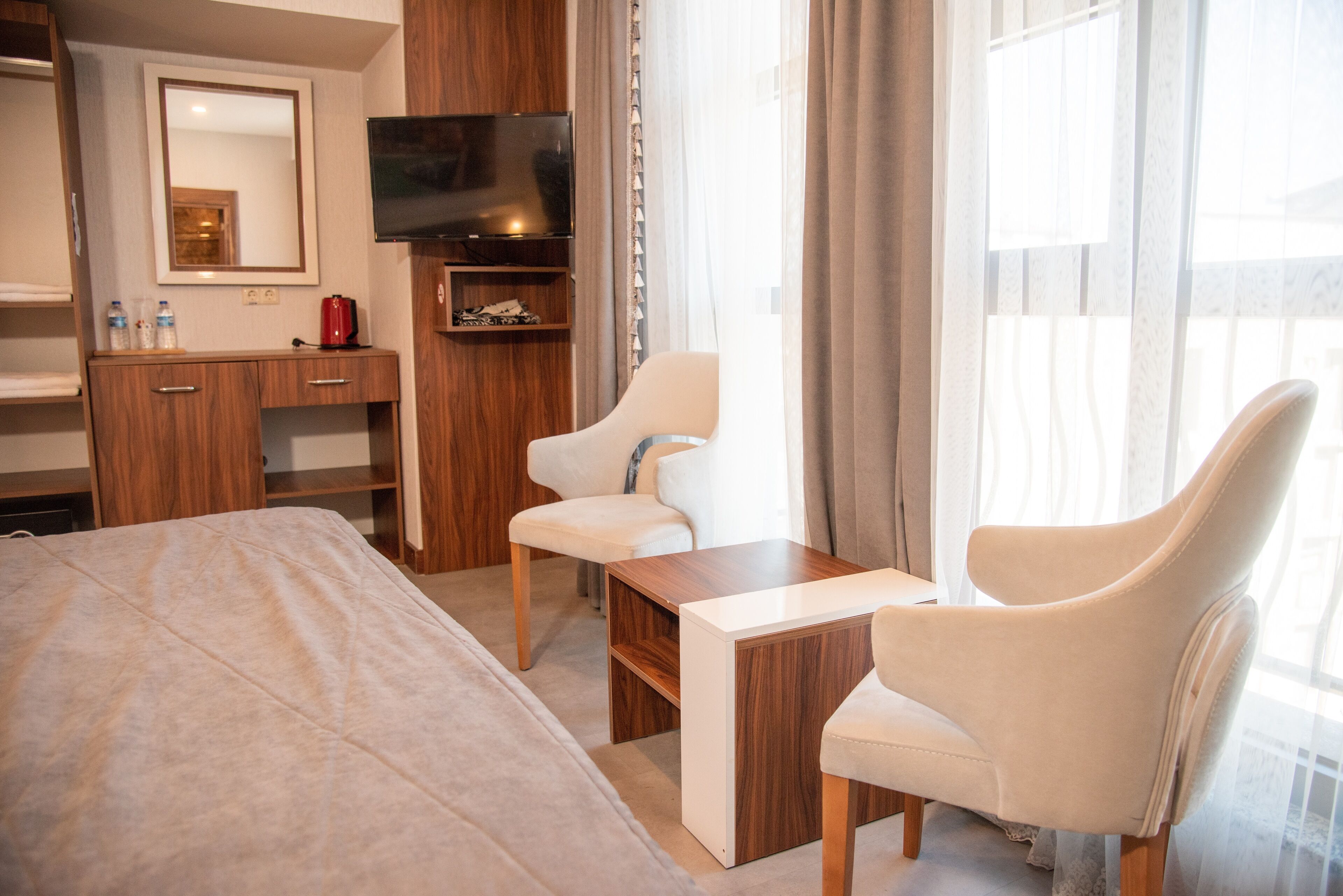A hotel room with a bed, a desk, two chairs, a TV, a mirror, and a window with curtains.