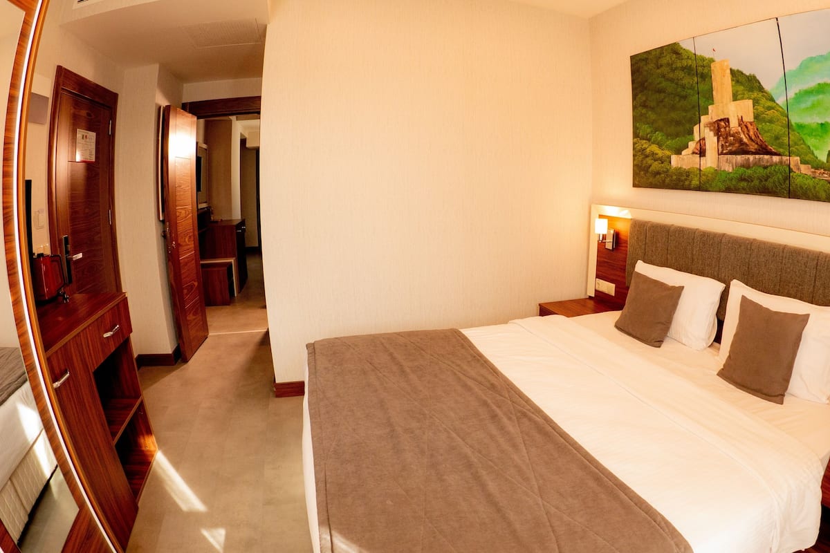 A hotel room with a large bed, wooden headboard, bedside tables with lamps, a painting on the wall, and a wooden wardrobe.