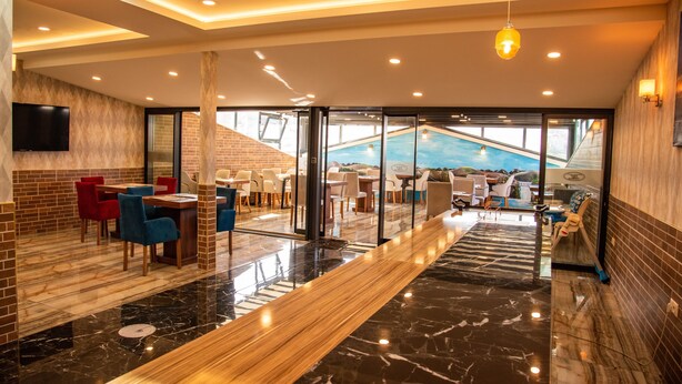 Un moderno vestíbulo de hotel con vista a la piscina, piso de madera y puertas de vidrio que dan al área de la piscina.