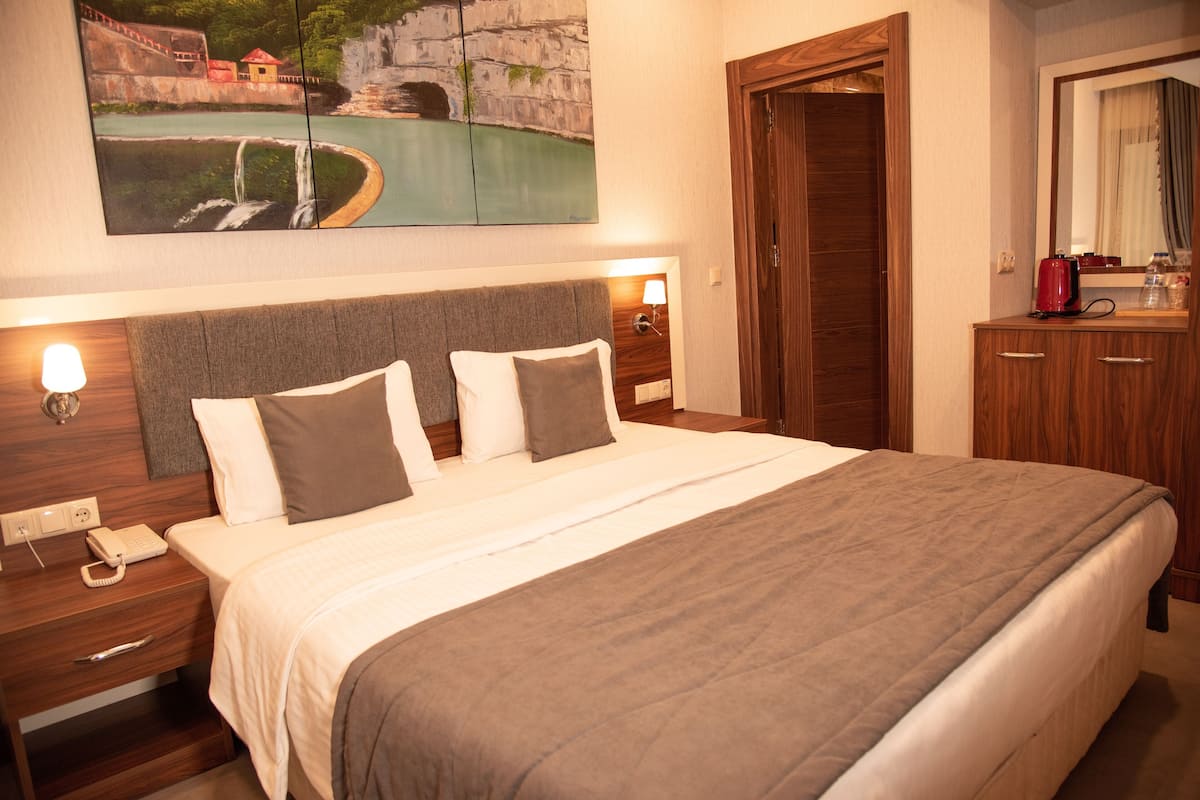 A hotel room with a large bed, a nightstand with a telephone, a wooden headboard, and a painting of a landscape above the bed.