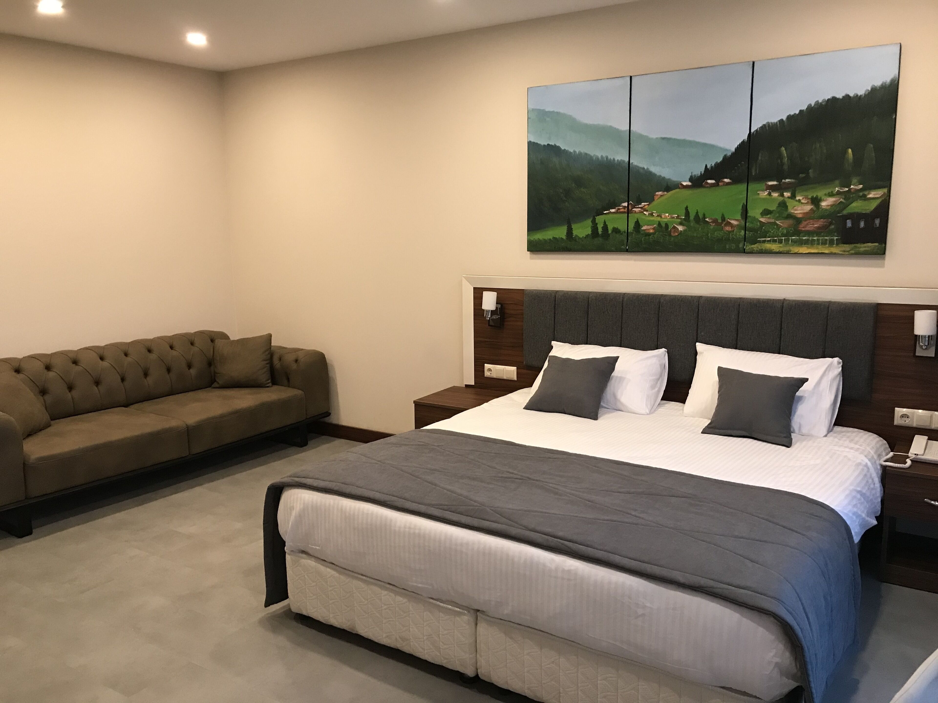 A bedroom with a large bed, a sofa, and a painting of a landscape.
