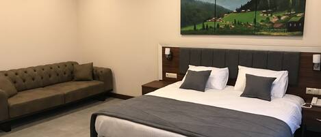 A bedroom with a large bed, a sofa, and a painting of a landscape.