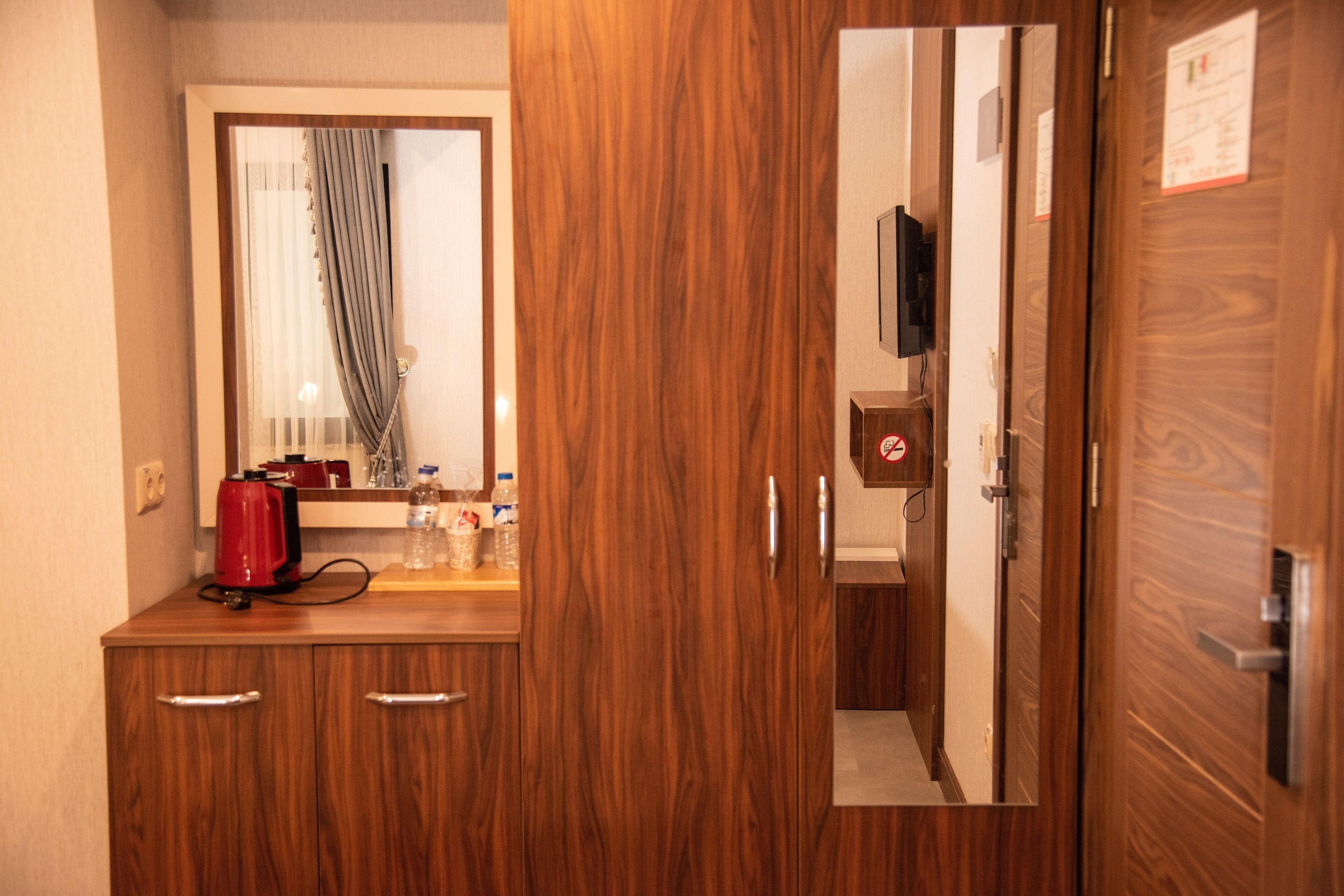 Un mueble de madera con un espejo, una tetera roja y una ventana con cortinas.
