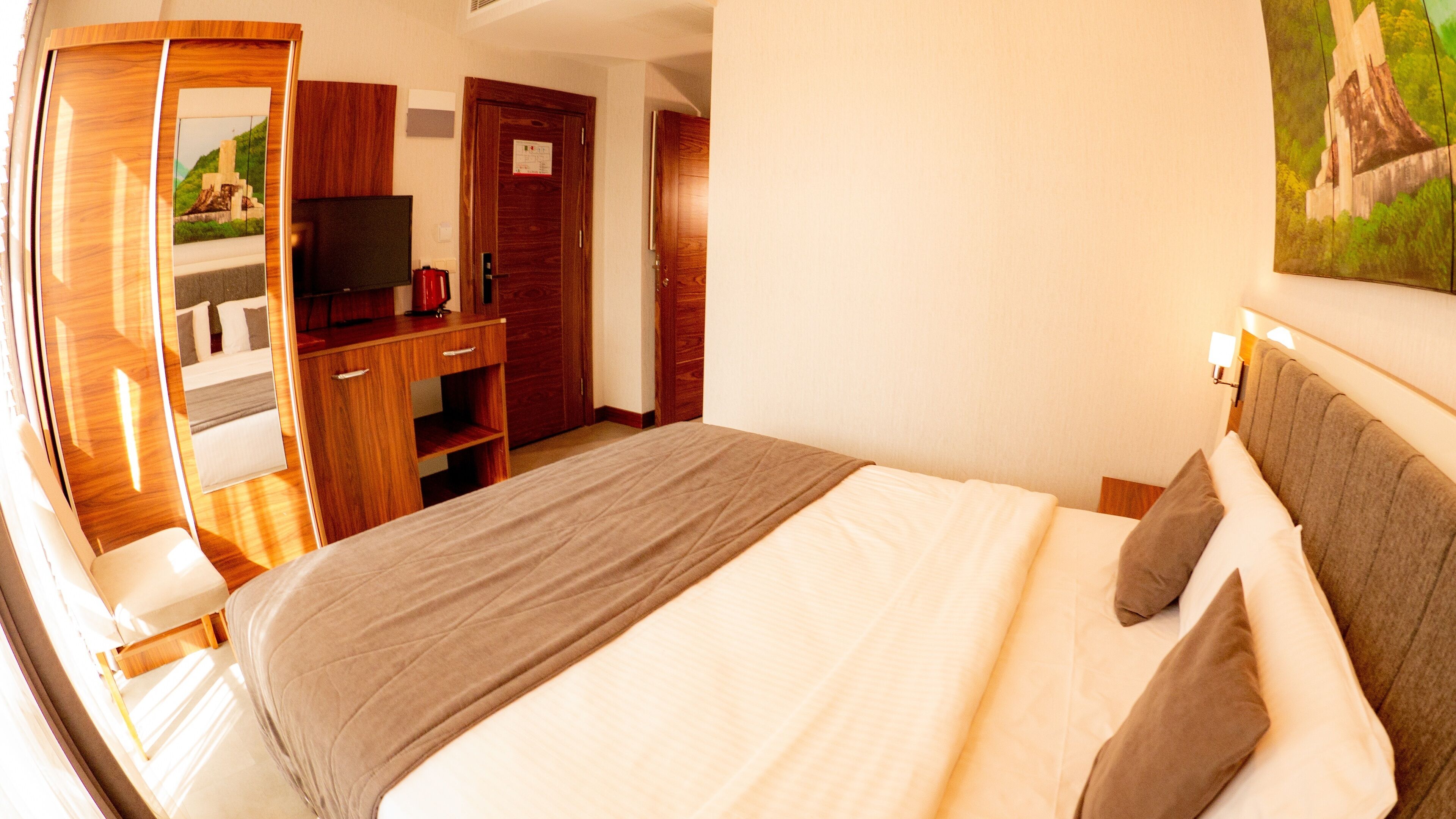 Ein Hotelzimmer mit einem großen Bett, Holzmöbeln, einem Fernseher und einem Gemälde an der Wand.