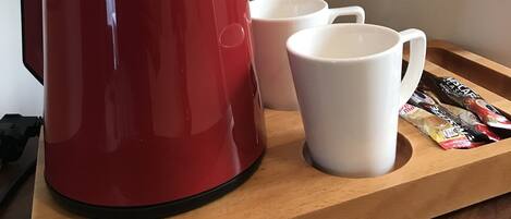 Una cafetera roja sobre una bandeja de madera con dos tazas blancas a un lado.
