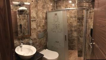 Baño con lavabo de mármol, inodoro y cabina de ducha de cristal.