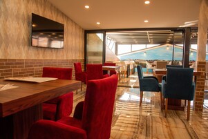 Un restaurante con sillas rojas y azules, una mesa de madera, un televisor montado en la pared y vistas a una piscina a través de grandes ventanales.