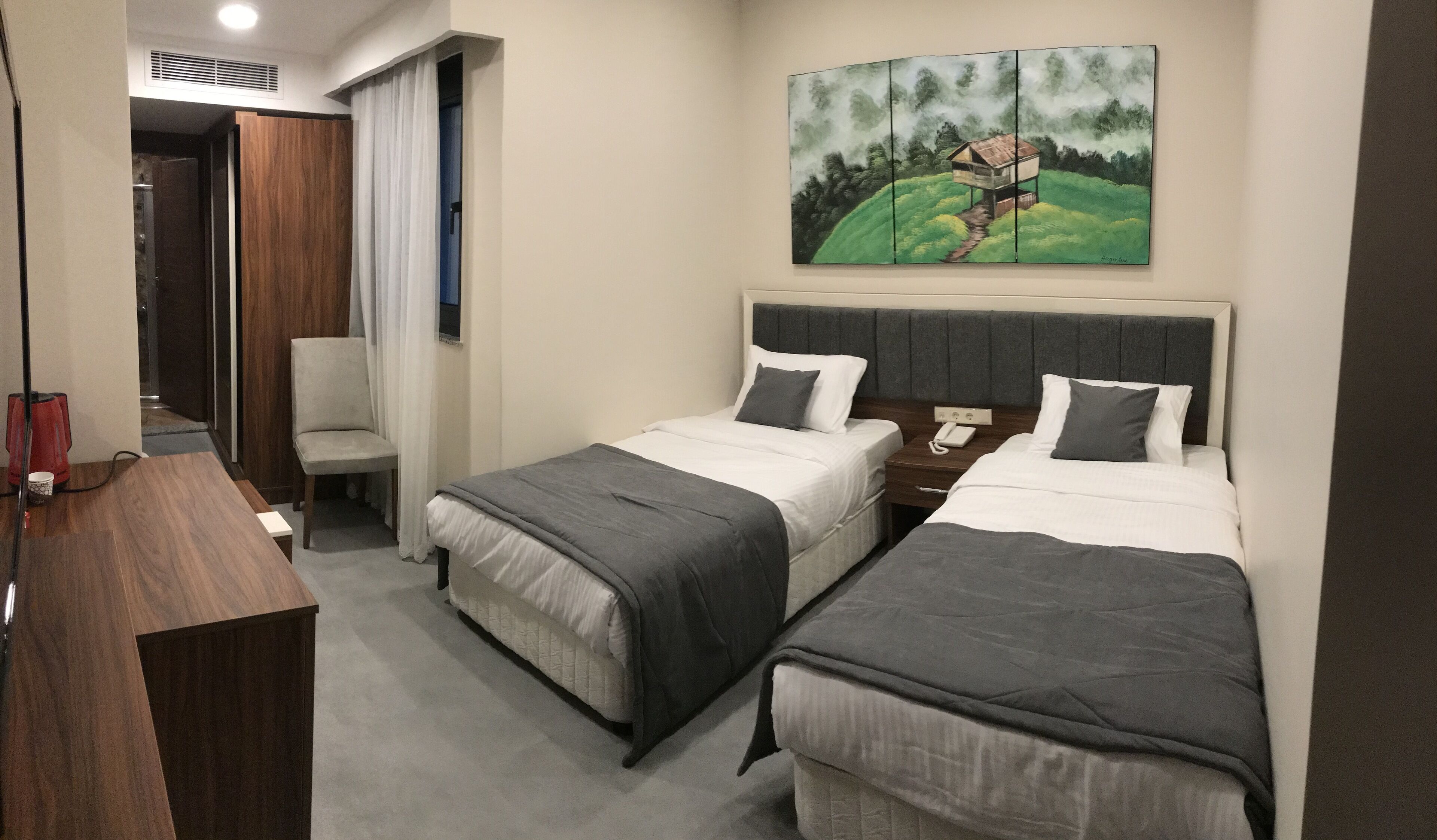 Ein Hotelzimmer mit zwei Betten, einem Schreibtisch, einem Stuhl und einem Gemälde an der Wand.