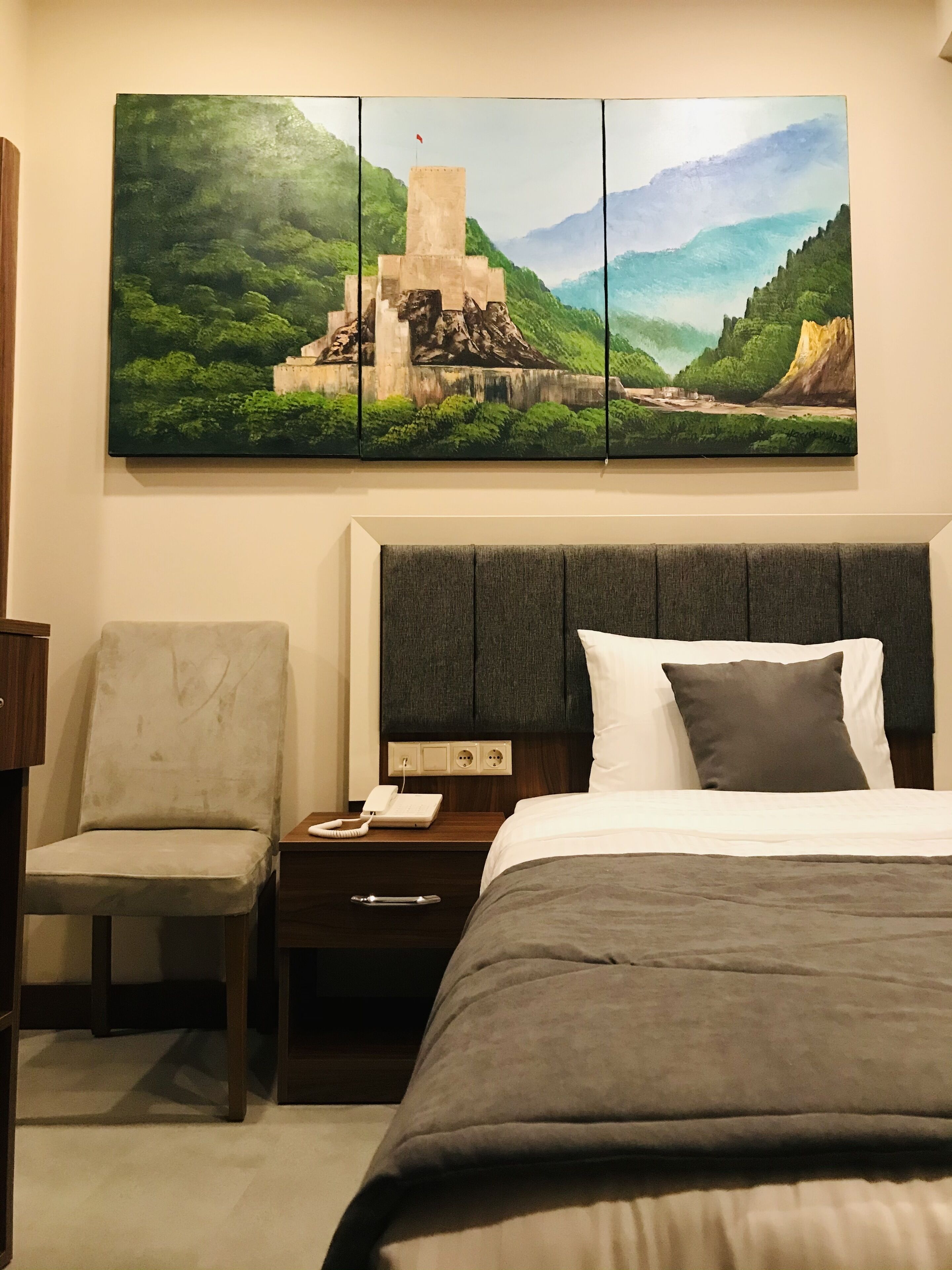 A hotel room with a bed, a chair, a nightstand, and a painting on the wall.