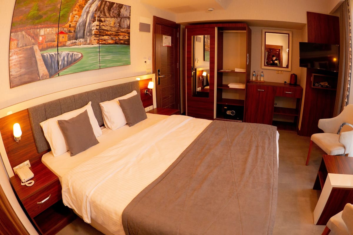 A hotel room with a large bed, a desk, a chair, a mirror, and a painting on the wall.