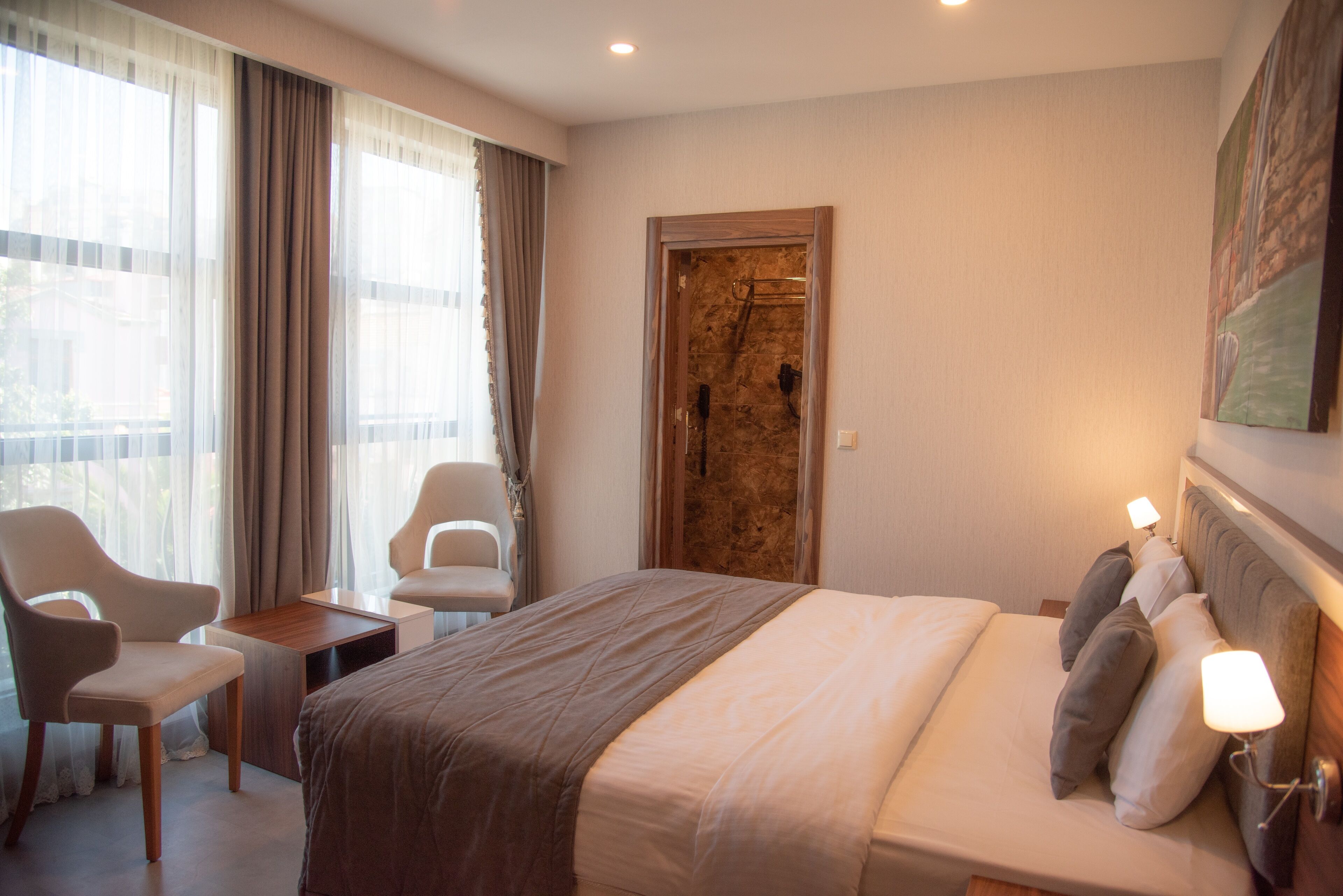 Una habitación de hotel con una cama grande, dos mesitas de noche, una silla y una puerta.