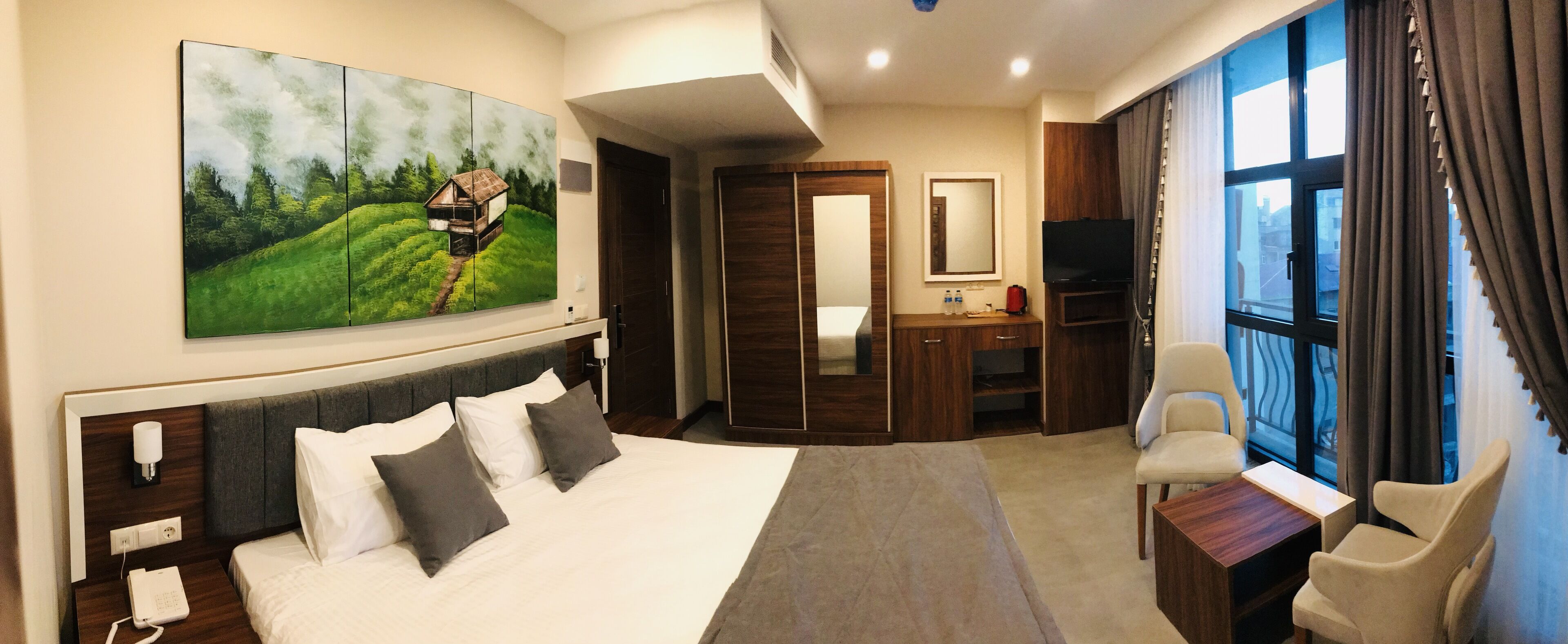 Habitación de hotel con una cama grande, un escritorio, una silla, un televisor y un cuadro en la pared.