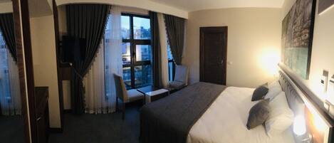 A hotel room with a large bed, a chair, a desk, and a TV.