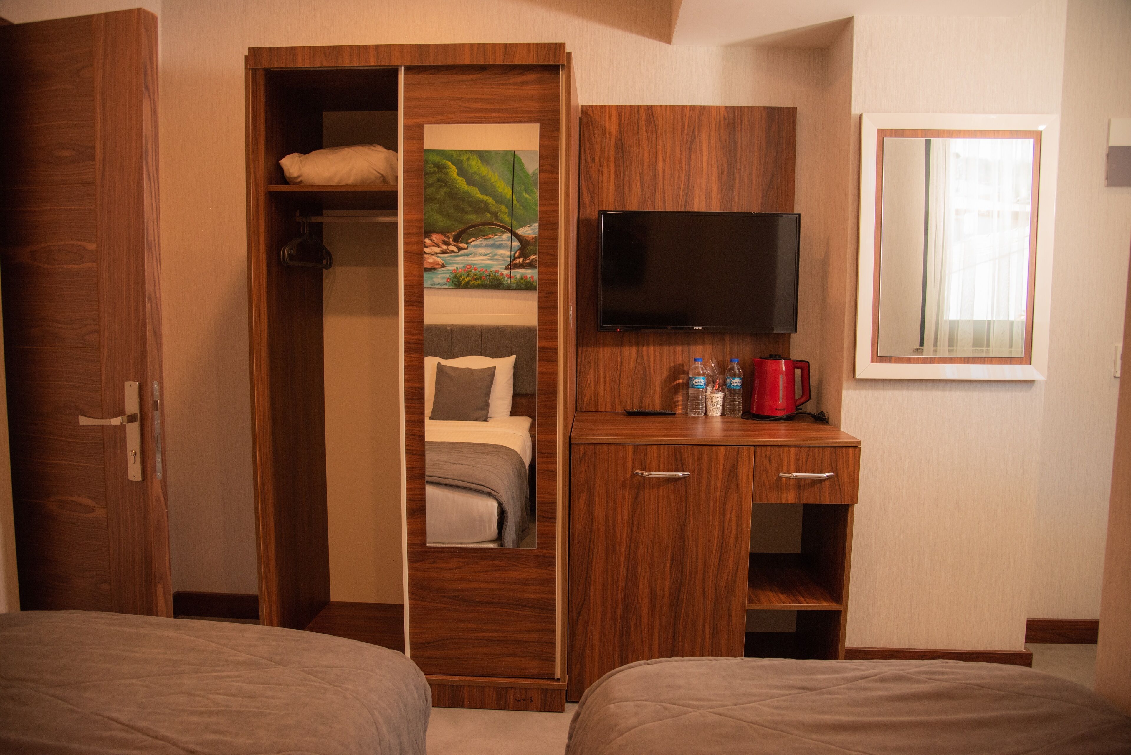 Habitación de hotel con armario de madera, una cama, un televisor y una pequeña mesa con una cafetera roja.