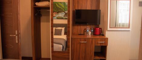 Habitación de hotel con armario de madera, una cama, un televisor y una pequeña mesa con una cafetera roja.